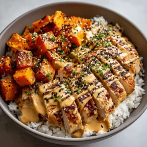 Wide shallow matte ceramic bowl filled with fluffy white rice, sliced warm spiced chicken, caramelized sweet potato cubes, and tahini sauce.