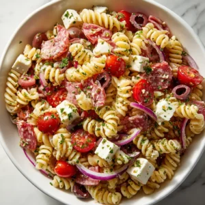 High-Protein Italian Pasta Salad That's Actually Filling 3 A close-up view of a High-Protein Italian Pasta Salad in a wide white ceramic bowl. The rotini pasta is mixed with salami, mozzarella, and tomatoes.