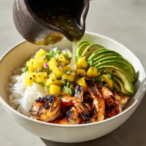 Shrimp and Avocado Bowls with Mango Salsa and Creamy Lime-Chili Sauce 3 Close-up of grilled shrimp with black char marks and fanned-out avocado slices in a bowl. (Shrimp and Avocado Bowls)