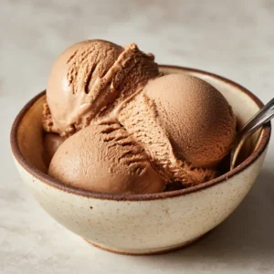A close-up eye-level shot of three scoops of creamy coffee gelato in a light beige speckled bowl. (Coffee Gelato)